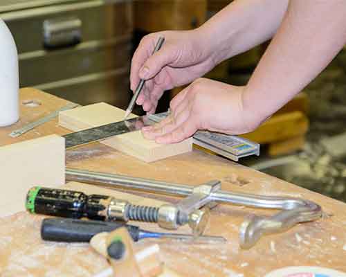 Carpenter marking a wooden board with a pencil and try square on a workbench